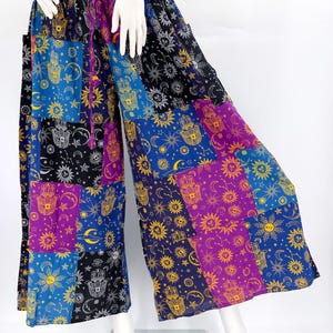 May include: Patchwork palazzo pants with a vibrant mix of colors including blue, purple, and black. The pants feature a repeating pattern of celestial symbols and Hamsa hand motifs. The wide-leg design is accentuated by a drawstring waist.