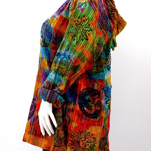 K&ouml;nnte beinhalten: Eine bunte, tie-dye bedruckte Kapuzenjacke mit Patchwork-Design, das verschiedene Symbole und Muster zeigt. Die Jacke ist aus einem weichen, leichten Stoff gefertigt und hat eine lockere Passform.