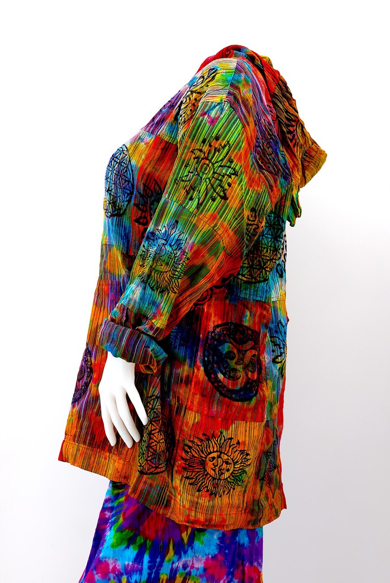 K&ouml;nnte beinhalten: Eine bunte, tie-dye bedruckte Kapuzenjacke mit Patchwork-Design, das verschiedene Symbole und Muster zeigt. Die Jacke ist aus einem weichen, leichten Stoff gefertigt und hat eine lockere Passform.