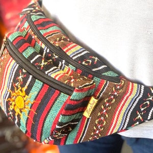 K&ouml;nnte beinhalten: Eine bunte, gestreifte Bauchtasche mit einem schwarzen Rei&szlig;verschluss und einem Sonnendesign. Die Bauchtasche hat ein braunes Leder-Etikett mit der Aufschrift "Himalaya".