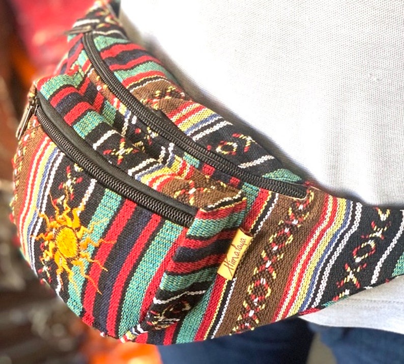 K&ouml;nnte beinhalten: Eine bunte, gestreifte Bauchtasche mit einem schwarzen Rei&szlig;verschluss und einem Sonnendesign. Die Bauchtasche hat ein braunes Leder-Etikett mit der Aufschrift "Himalaya".