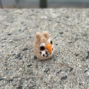 Puede incluir: Un pequeño búho de fieltro marrón y blanco con pico naranja y ojos negros.