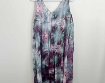 May include: A sleeveless midi dress featuring a tie-dye pattern in shades of deep plum, muted teal, and soft white. The garment has a V-neckline, wide shoulder straps, and a relaxed, flowing silhouette that hangs straight from the shoulders.
