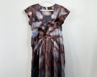 May include: A knee-length dress featuring a tie-dye pattern in shades of brown, black, and muted blue. The garment has short flutter sleeves, a round neckline, and a tiered skirt design, hanging from a white plastic hanger against a plain wall.