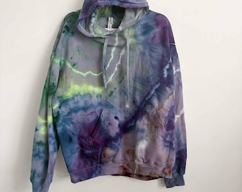 May include: A long-sleeve hooded sweatshirt featuring a tie-dye pattern in shades of purple, blue, green, and hints of yellow. The garment includes a front kangaroo pocket, a drawstring hood, and ribbed cuffs at the sleeves and bottom hem.