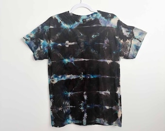May include: A short-sleeve crew neck t-shirt featuring a tie-dye pattern with horizontal bands of black, deep blue, and white. The fabric displays a dark, moody aesthetic with concentrated areas of color saturation and lighter, faded sections.