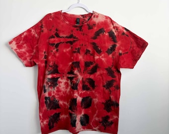 May include: A short-sleeve crew neck t-shirt featuring a tie-dye pattern in shades of vibrant red and deep black. The garment displays a repeating geometric-like motif created by the dye process, with a consistent color distribution across the fabric.