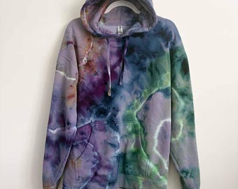 May include: A long-sleeve hooded sweatshirt featuring a tie-dye pattern in shades of purple, blue, and green. The garment includes a front kangaroo pocket, a drawstring hood, and ribbed cuffs at the sleeves and hem, showcasing a blended color effect.