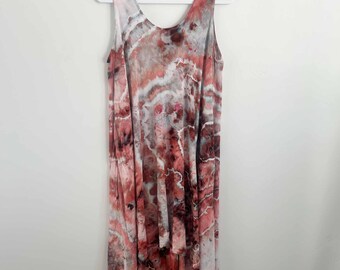 May include: A sleeveless dress featuring a tie-dye pattern in shades of coral, dusty rose, white, and dark charcoal gray. The garment has a scoop neckline and an asymmetrical hemline that is shorter in the front and longer in the back.