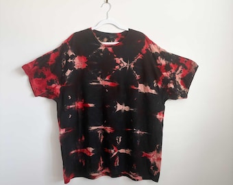 May include: A short-sleeve t-shirt featuring a black base color with a tie-dye pattern in shades of red and light pink. The garment has a crew neckline and a relaxed fit, displaying a repeating abstract design across the front surface.
