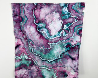 May include: A square textile featuring a tie-dye pattern with swirling layers of deep magenta, soft lavender, and teal green. The design mimics the concentric, organic bands of a geode, with thin white lines separating the saturated color fields.