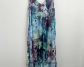 May include: A sleeveless dress featuring a tie-dye pattern in shades of deep purple, navy blue, teal, and light blue. The garment has a V-neckline and a high-low hemline, with a longer back section that drapes below the front hem.