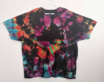 May include: A short-sleeve t-shirt featuring a black base with a vibrant tie-dye pattern in shades of magenta, bright orange, yellow, and turquoise. The design displays a swirling, multi-colored spiral effect across the fabric, creating a bold contrast against the dark background.