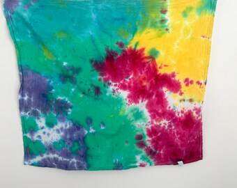 May include: A vibrant tie-dye textile in shades of teal, purple, green, yellow, and magenta. The fabric is rectangular and appears to be a scarf or a similar accessory. The colors blend and swirl, creating a unique pattern.