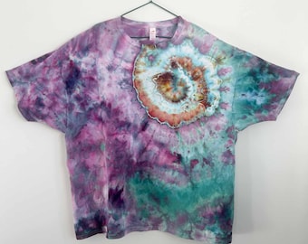 May include: A short-sleeve t-shirt featuring a tie-dye pattern in shades of purple, teal, and magenta. The shirt displays a prominent circular spiral design on the upper right chest area, showcasing concentric rings of brown, orange, and white hues.