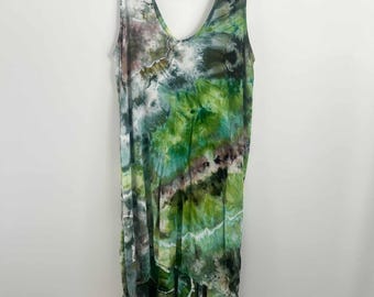 May include: A sleeveless dress featuring a tie-dye pattern in shades of forest green, lime, white, and dark charcoal. The garment has a deep V-neckline and an asymmetrical hemline that is longer in the back, hanging on a white plastic hanger.