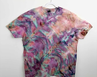 May include: A short-sleeve crew neck t-shirt featuring a multi-colored tie-dye pattern. The fabric displays a blend of vibrant pink, purple, teal, and soft peach hues swirled together in an abstract design across the entire garment surface.
