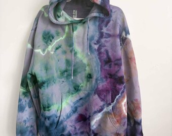 May include: A long-sleeve hooded sweatshirt featuring a tie-dye pattern in shades of purple, blue, green, and hints of orange. The garment includes a front kangaroo pocket, a drawstring hood, and ribbed cuffs at the sleeves and bottom hem.