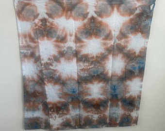 May include: A square fabric cloth featuring a tie-dye pattern with repeating circular motifs in shades of rust orange, slate blue, and charcoal gray against a white background, creating a symmetrical, abstract design across the entire surface.