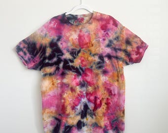 May include: A short-sleeve crew neck t-shirt featuring a vibrant tie-dye pattern in shades of magenta, deep purple, and golden yellow. The garment displays a swirling, abstract color blend across the front and back, hanging on a white hanger.