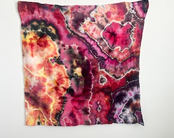 May include: A square textile piece featuring a vibrant tie-dye pattern in shades of magenta, deep purple, black, and golden yellow. The design displays organic, swirling shapes with intricate, vein-like white lines throughout the fabric surface.