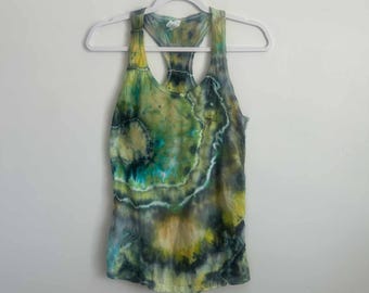 May include: A sleeveless racerback tank top featuring a tie-dye pattern in shades of forest green, lime yellow, and deep charcoal. The design displays concentric circular shapes with white accents, creating a fluid, organic aesthetic across the fabric.