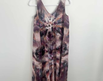 May include: A sleeveless midi dress featuring a V-neckline and a tie-dye pattern in shades of deep purple, charcoal gray, muted brown, and soft white. The garment hangs straight from the shoulders with a relaxed fit and an uneven hemline.