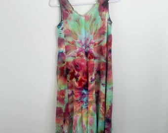 May include: A sleeveless dress featuring a vibrant tie-dye pattern with blended shades of pink, teal, yellow, and purple. The garment has a V-neckline and a flowing, asymmetrical hemline that hangs longer in the center, displayed on a white hanger.