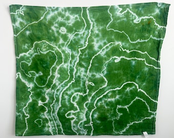 May include: A square fabric cloth featuring a tie-dye pattern in shades of forest green and white. The design consists of organic, flowing white lines that create a topographical or marble-like effect against the deep green background.