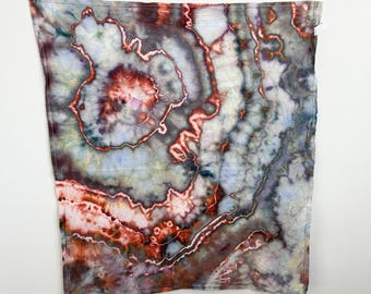 May include: A square textile featuring a geode-inspired tie-dye pattern with concentric rings of deep rust, burnt orange, and muted gray. The design incorporates soft white and pale blue gradients, creating a complex, organic, and layered appearance.