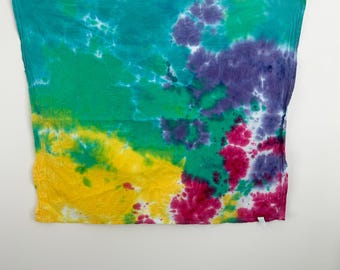 May include: A tie-dye textile with a vibrant mix of colors, including teal, green, yellow, purple, and pink. The fabric has a soft, textured appearance, with the colors blending in a unique pattern. The textile is displayed against a white background.