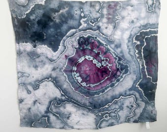 May include: A square textile featuring a tie-dye pattern with a central spiral in shades of deep magenta and purple, surrounded by concentric, organic rings of dark charcoal, slate gray, and white, resembling the appearance of a sliced geode.