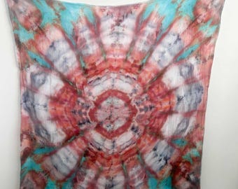May include: A square scarf featuring a tie-dye pattern with a central circular motif. The design radiates outward in shades of coral, deep red, and dark gray, contrasted against a bright turquoise background, creating a symmetrical effect.