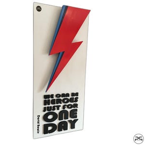 Può includere: Un'opera d'arte murale rettangolare bianca con un fulmine rosso e blu. Il testo "WE CAN BE HEROES JUST FOR ONE DAY" e "David Bowie" sono in lettere nere in 3D.