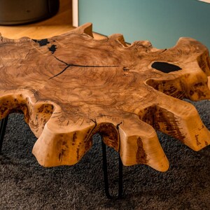 Può includere: Un tavolino da caffè unico con bordo vivo. Il tavolo è realizzato con un unico pezzo di legno marrone chiaro con una forma naturale e organica. Presenta crepe riempite di resina nera e poggia su gambe a forcina in metallo nero. Misura circa 122 cm di lunghezza.