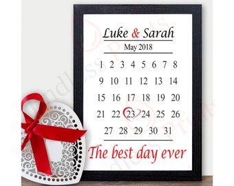 May include: A black framed print with a white background. The print features a calendar with the date May 23, 2018 circled in red. The text "Luke & Sarah" and "The best day ever" are printed on the calendar.