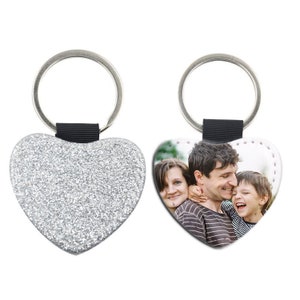 May include: Silver glitter heart-shaped keychain with a black strap and a silver metal ring. The back of the keychain features a photo of a family of three.