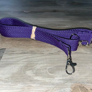 May include: Purple adjustable strap with two silver swivel clasps. The strap is made of woven nylon.