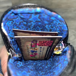 May include: A small black zipped pouch with a vibrant blue interior lining featuring a repeating star pattern. Inside the pouch, a rectangular business card is visible, displaying the text Artistic Attitude and a QR code on a wood-grain background.