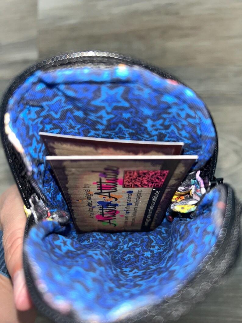 May include: A small black zipped pouch with a vibrant blue interior lining featuring a repeating star pattern. Inside the pouch, a rectangular business card is visible, displaying the text Artistic Attitude and a QR code on a wood-grain background.