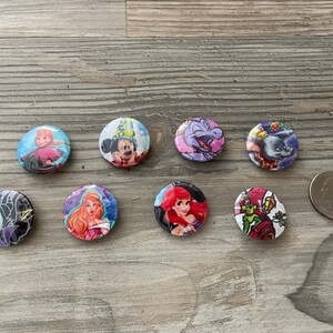 May include: Eight round buttons with different Disney characters. The buttons are colorful and feature characters like Mickey Mouse, Ariel, and Maleficent.