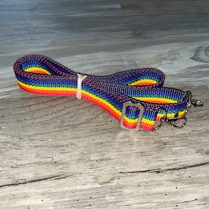 May include: A rainbow striped adjustable strap with silver hardware. The strap is made of woven nylon and has a red, orange, yellow, green, blue, and purple color scheme.