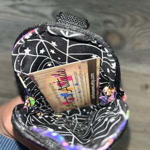 May include: A small, zippered pouch with a black interior lining featuring a white spiderweb and star pattern. Inside the pouch is a rectangular business card with the text Artistic Attitude, social media handles, and steffaniesews.etsy.com.
