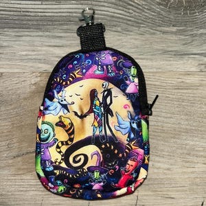 May include: A small zippered pouch featuring a colorful print of characters from The Nightmare Before Christmas, including Jack Skellington and Sally standing before a large yellow moon, with a black fabric trim and a metal lobster claw clasp.