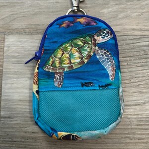 May include: A small blue zippered pouch with a sea turtle design. The pouch has a turquoise fabric lining and a silver key ring.