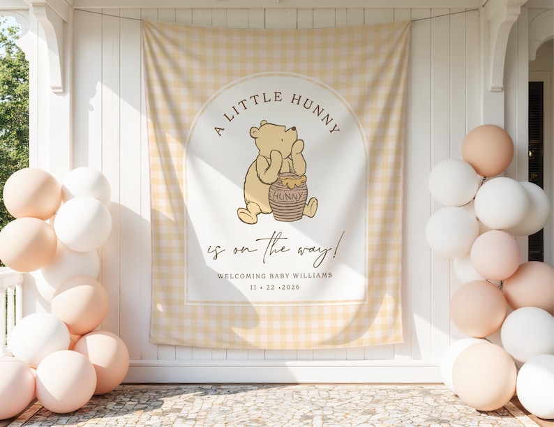 A mockup of a winnie the pooh baby shower photo backdrop. The backdrop shows a cute winnie the pooh graphic with soft yellow gingham with the words "a little hunny is on the way". On the bottom of the banner, there is a section where a custom name and date can be added.