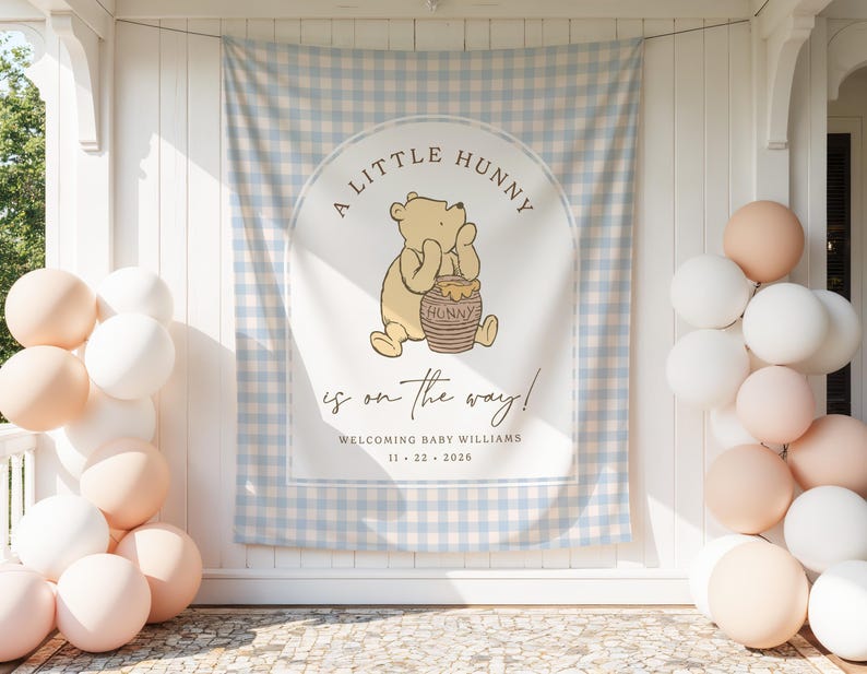 May include: A rectangular fabric backdrop featuring a light blue and white gingham pattern with a central arch design. It displays a yellow bear illustration holding a honey pot, with the text A LITTLE HUNNY is on the way! WELCOMING BABY WILLIAMS 11 22 2026.