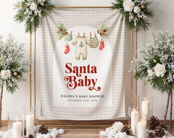 May include: A baby shower banner with a beige gingham design. It features a watercolour illustration of baby clothes and the text "Santa Baby." The banner is framed by floral arrangements and candles, creating a warm, celebratory atmosphere.