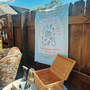 May include: A picnic scene with a woven basket, a sign that says "Fresh Off The Market", and a floral patterned chair. The sign is hanging on a wooden fence. The scene is set outdoors.