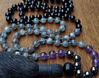 May include: A black, gray, and purple beaded necklace with a tassel. The necklace is made of various stones, including black onyx, labradorite, and amethyst.